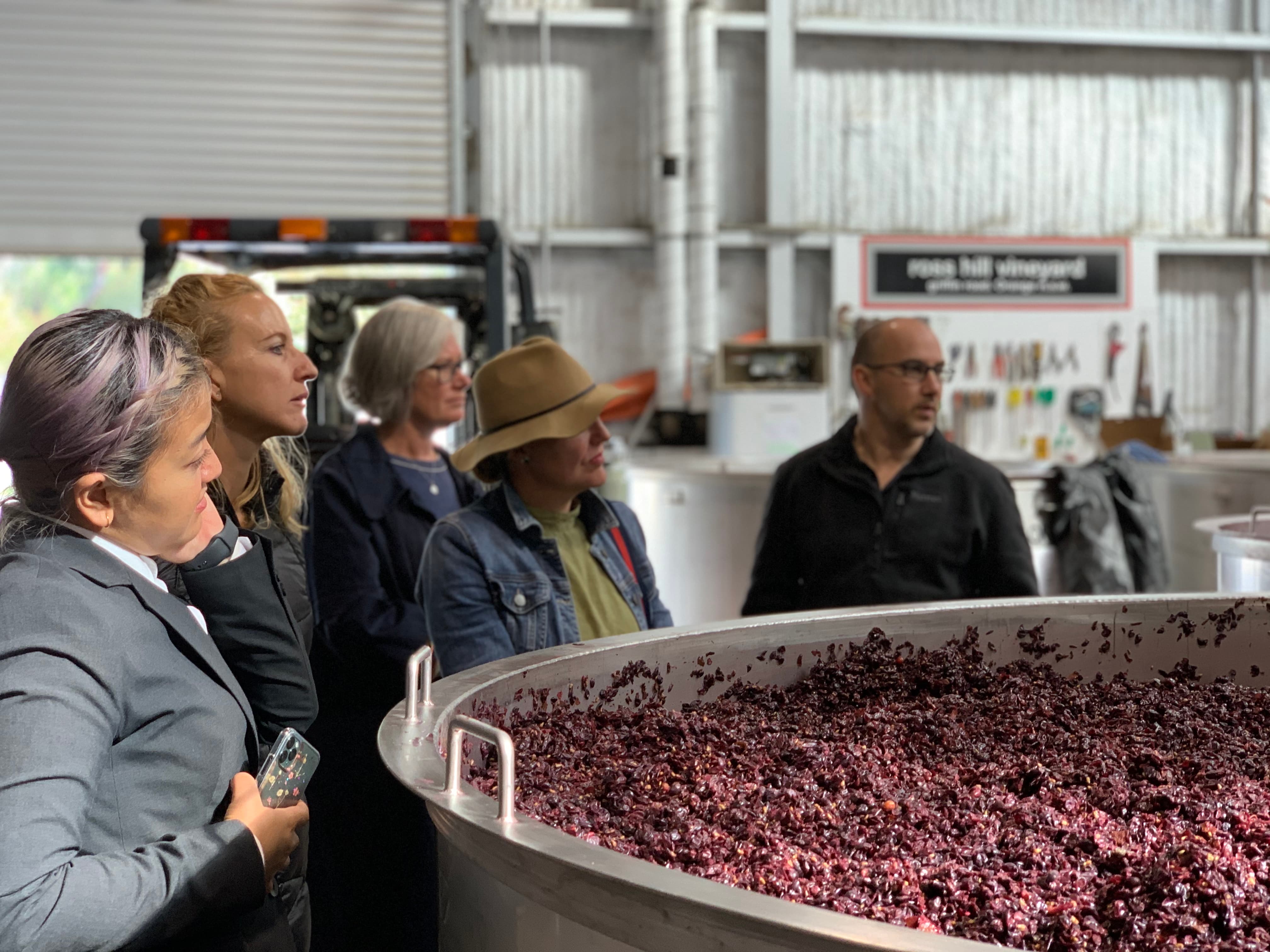 5 peopel standing near vat of wine